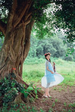 Kız büyük ağacın altında keman çalıyor.