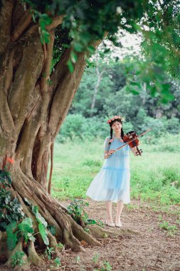 Kız büyük ağacın altında keman çalıyor.