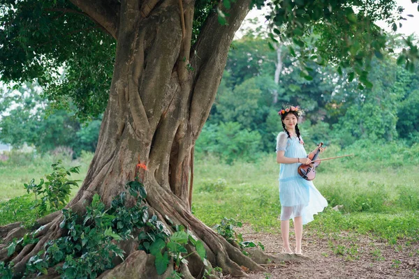 女の子は大きな木の下でバイオリンを弾いている — ストック写真
