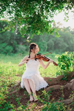 Kız büyük ağacın altında keman çalıyor.