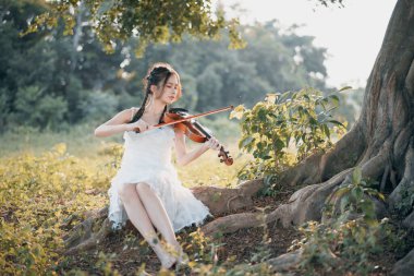 Kız büyük ağacın altında keman çalıyor.