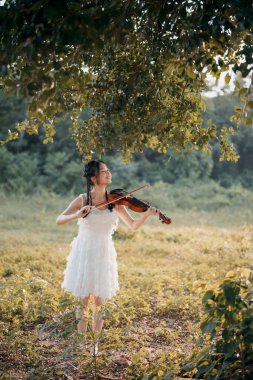 Kız büyük ağacın altında keman çalıyor.