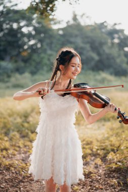 Kız büyük ağacın altında keman çalıyor.