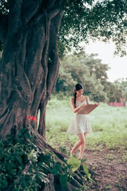 Kız büyük ağacın altında çizim yapıyor.