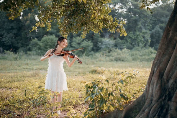 stock image The girl is playing the violin under the big tree