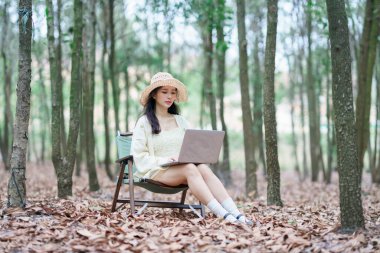 Kız ormanda dizüstü bilgisayar kullanıyor.