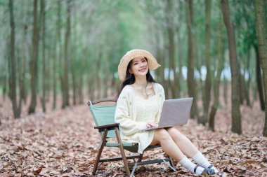 Kız ormanda dizüstü bilgisayar kullanıyor.