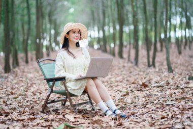 Kız ormanda dizüstü bilgisayar kullanıyor.