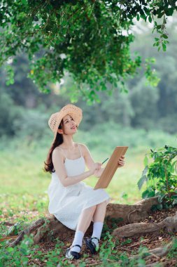 Kız büyük ağacın altında çizim yapıyor.