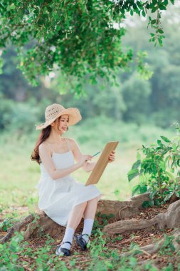 Kız büyük ağacın altında çizim yapıyor.