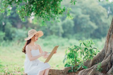 Kız büyük ağacın altında çizim yapıyor.