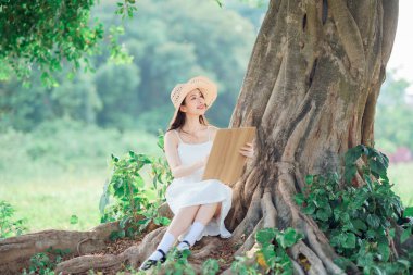 Kız büyük ağacın altında çizim yapıyor.