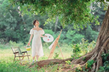 Kız büyük ağacın altında çizim yapıyor.