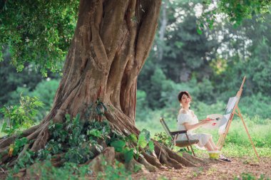 Kız büyük ağacın altında çizim yapıyor.