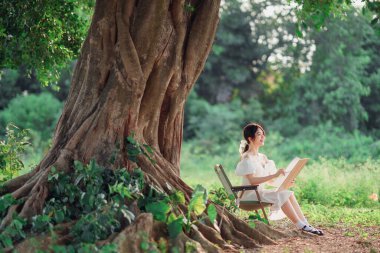 Kız büyük ağacın altında çizim yapıyor.
