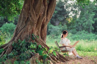 Kız büyük ağacın altında çizim yapıyor.