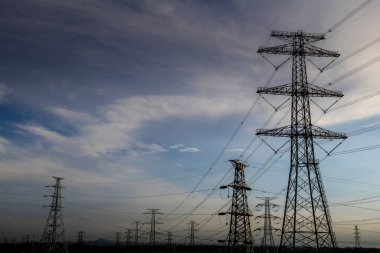 Elektrik iletim pilonu alacakaranlıkta mavi gökyüzüne karşı siluetlendi