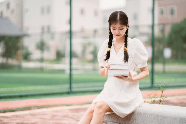 Bayan bir üniversite öğrencisi kampüste kitap tutuyor.