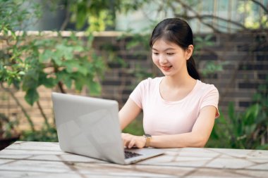 Kız bahçede dizüstü bilgisayar kullanıyor.