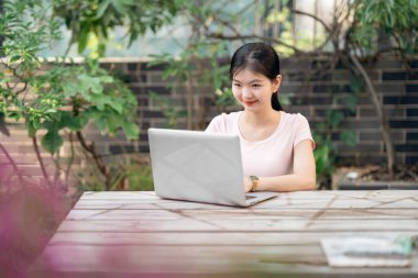 Kız bahçede dizüstü bilgisayar kullanıyor.