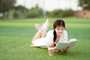 Bayan bir üniversite öğrencisi kampüste kitap tutuyor.