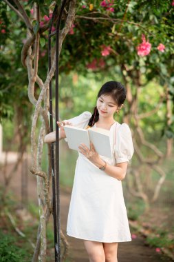 Bayan üniversite öğrencileri parkta kitap okurlar.