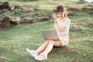 Kız çimlerde dizüstü bilgisayar kullanıyor.