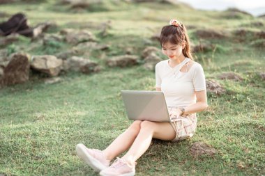 Kız çimlerde dizüstü bilgisayar kullanıyor.