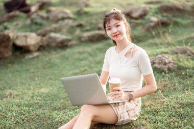 Kız çimlerde dizüstü bilgisayar kullanıyor.