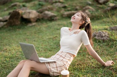 Kız çimlerde dizüstü bilgisayar kullanıyor.
