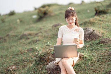 Kız çimlerde dizüstü bilgisayar kullanıyor.