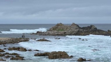 Pasifik Korusu, California yakınlarındaki Pasifik Okyanusu 'na bakan Monterey Körfezi' nin geniş bir manzarası. Dalgalar arka plandaki kayalara çarptığında turistler uzaktan görülebilir. Kamera kilitlendi..