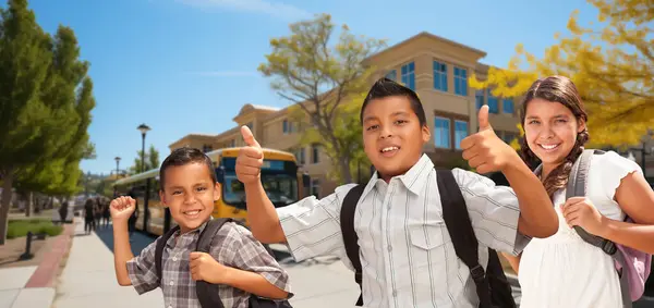 stock image Excited Young Hispanic Boy Wearing a Backpack Giving Two Thumbs Up Surrounded by His Friends on Campus