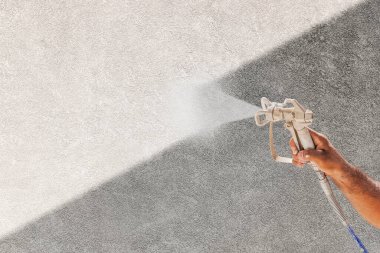 Profesyonel sprey boya tutucu sprey tabanca Gri Stucco yüzeyine beyaz boya püskürtüyor.