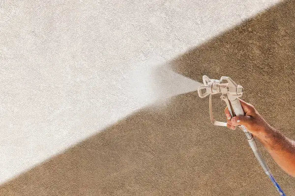 ブラウン スチュコ 表面上の白いペンキを吹くスプレーガンを握る専門のスプレー ペインター — ストック写真