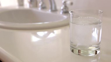 Slow Motion Effervescent Soğuk algınlığı hapları lavabonun yanındaki su bardağına düşüyor..