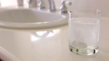 Slow Motion Woman soğuk algınlığı haplarını lavabo yanındaki bir su bardağına düşürdü..