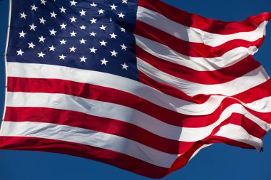 Derin mavi gökyüzüne karşı rüzgarda dalgalanan Amerikan Bayrağı.
