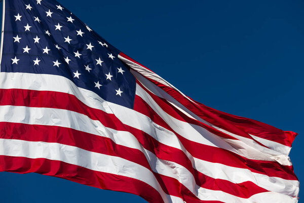 American Flag Waving In The Wind Against Deep Blue Sky.