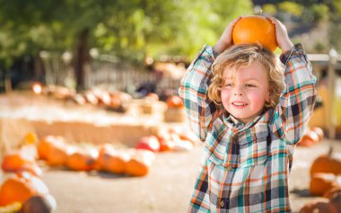 Güneşli bir sonbahar gününde balkabağı tarlasında eğlenen sevimli genç çocuk.