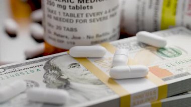 Reçeteli ilaç şişeleri ve haplar 100 dolarlık banknotların yanında..