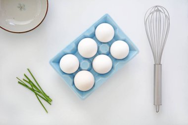 Mavi seramik yumurta kartonunda taze beyaz jumbo yumurtalar çırpılmış, soğan soğanı ve düz kompozisyonda kâse. Beyaz arkaplanda sağlıklı malzemeler