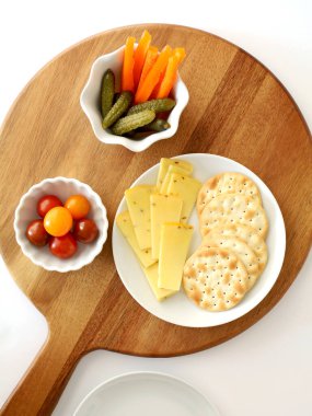 Dutch Gouda cheese slices and water crackers with cherry tomatoes,orange pepper strips and gherkins on round wooden serving board in flat lay composition.