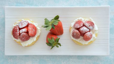 Fresh sweet strawberries with whipped cream on yellow sponge dessert cups in flat lay composition in horizontal format.