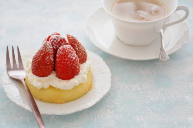 Fresh sweet strawberries with whipped cream on yellow sponge dessert cup and cup of tea in horizontal format