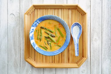 Spicy Thai red curry soup with asparagus on bamb oo tray for a healthy, warming meal in flat lay composition.