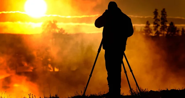 摄影师用三脚架和相机拍摄日出或日落与蒸汽和树木 — 图库照片