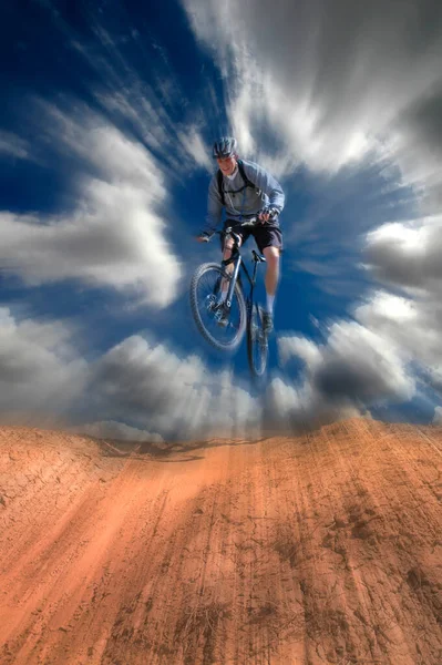 Man mountain biking on trail in outdoors jumping on dirt with sky and zoom motion