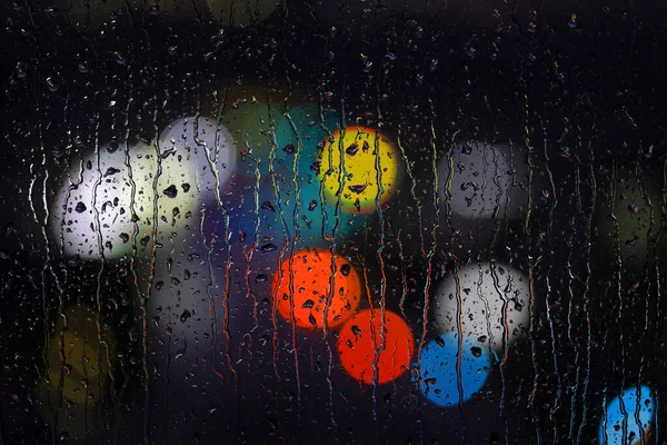 Rainy wet window at night with water drops and colorful city lights