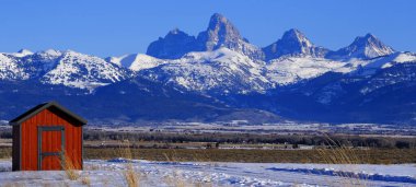 Kışın Grand Teton Dağı Dağları 'nın önündeki kırmızı ahır inşaatı ya da kulübesi